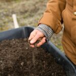 person in yellow jacket holding black soil