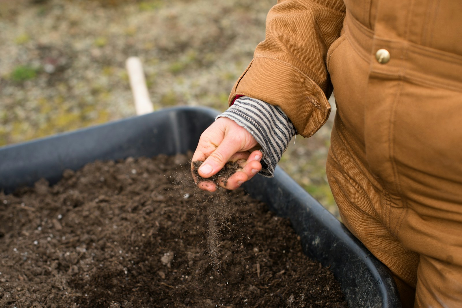 person in yellow jacket holding black soil