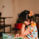 a little girl sitting at a table with a book