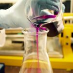 person pouring purple liquid on clear glass container