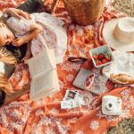 woman reading with girl while lying on orange and white floral picnic mat