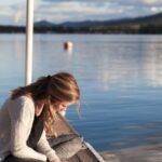 photo of woman reading book near body of water