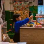 boy in blue long sleeve shirt standing beside brown wooden table